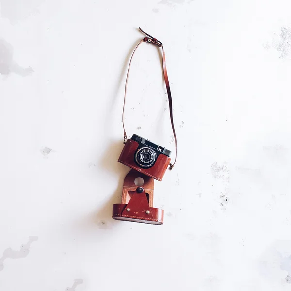 Vintage film camera hanging on grunge white wall, filtered photo
