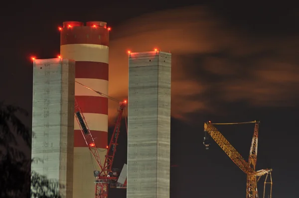 Power lights illuminated at night. Chimneys launching smoke. Cranes, extending the electron. Heat generation. United factory.
