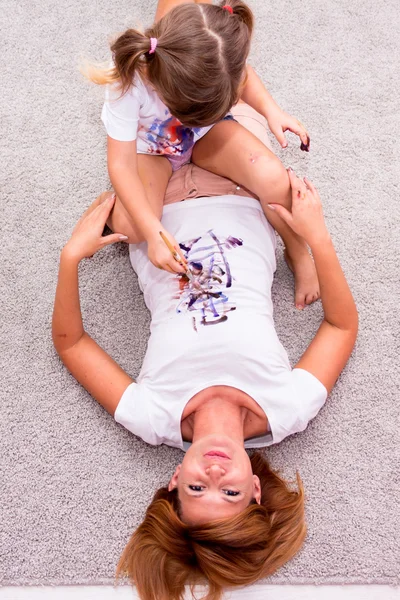 Girl draws paints on a T-shirt mother lying on the floor.