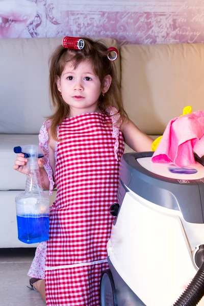 Little girl stands near a vacuum cleaner.