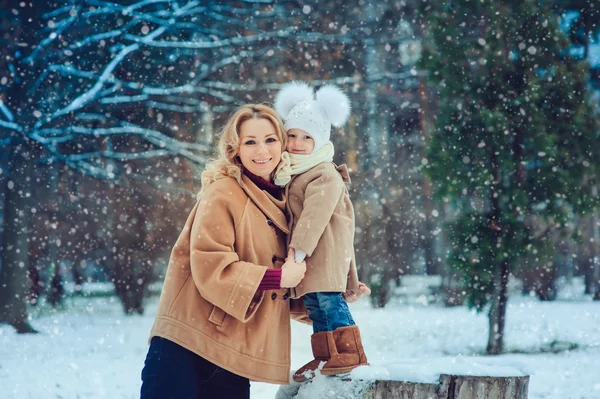 Happy mother and baby daughter walking in snowy winter park. Christmas family time.