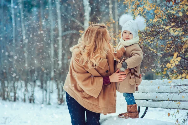 Happy mother and baby daughter walking in snowy winter park. Christmas family time.