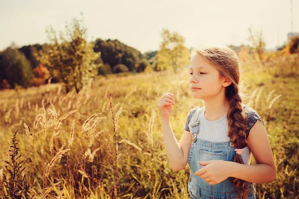 Happy child girl in jeans overall playing on sunny field, summer outdoor lifestyle, cozy mood