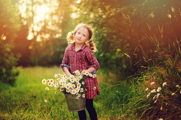 Cute child girl picking flowers outdoor on summer field, cozy mood, rural scene