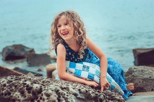 Happy child girl relaxing on the beach, wrapped in cozy quilt blanket