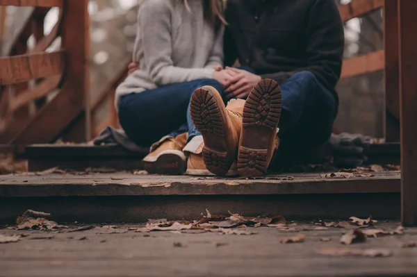 Boots of young loving couple walking outdoor on wooden bridge in autumn