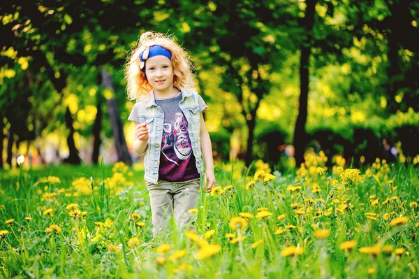 Happy child girl playing on colorful spring field. Blooming dandelions on background, outdoor seasonal activities. Cozy warm mood.