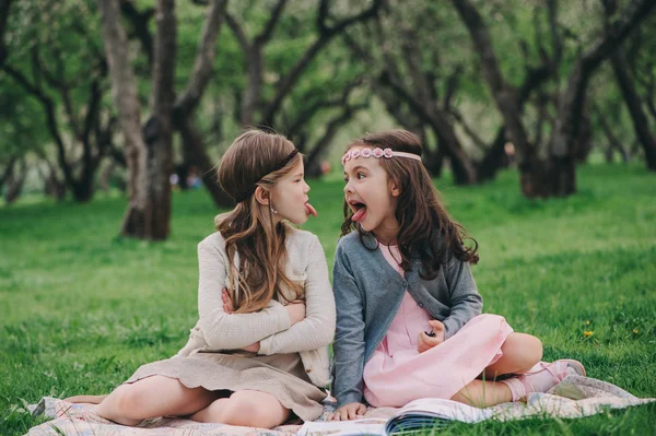 Two kid girlfriends showing tongue to each other on the walk in spring. Upset angry sisters. Outdoor activities.