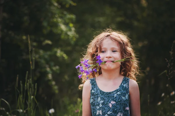 Happy child girl playing with bouquet of bluebells in summer. Happy childhood, outdoor activities. Exploring nature and picking flowers. Cozy country vacations.