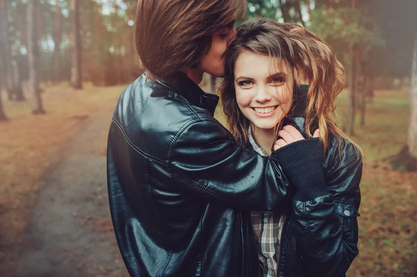 Young happy loving couple in leather jackets hugs outdoor on cozy walk in forest
