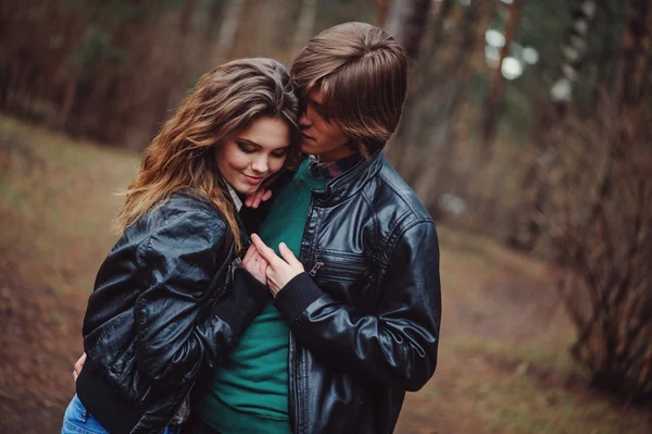 Happy loving couple in leather jackets walking outdoor. Young boyfriend and girlfriend hugs and kissing in the forest