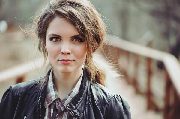 Outdoor portrait of adorable young woman in leather jacket and plaid skirt. Soft warm toned, cozy mood.