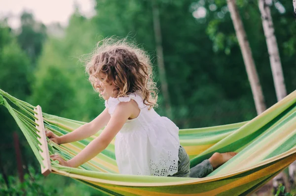 Happy child girl relaxing in hammock on summer camp in forest. Outdoor seasonal activities for kids.