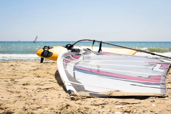 Windsurfing board with sail lying on the sand