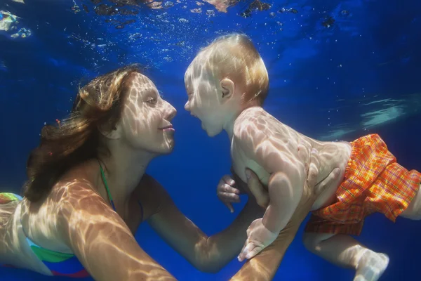 Little child swimming underwater in pool with mother