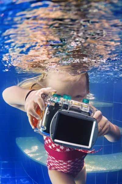 Little child with camera takes underwater photo in pool.