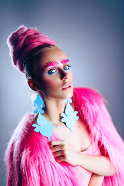 Girl model with blue eyes in a pink coat and blue earrings. Art hairstyle and makeup. On a blue background.