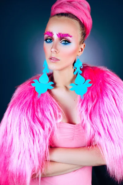 Girl model with blue eyes in a pink coat and blue earrings. Art hairstyle and makeup. On a blue background.