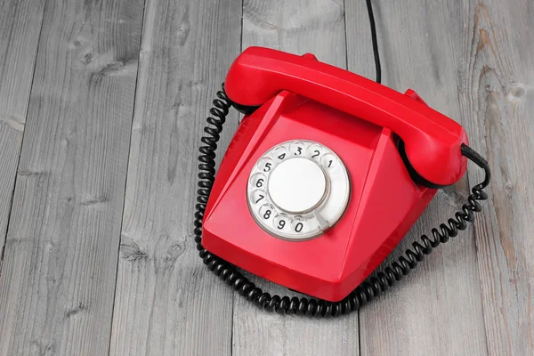 Red retro rotary phone on a wooden platform.