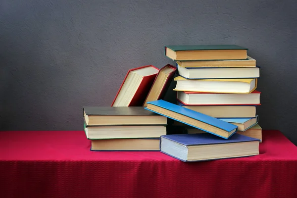 A stack of books on the table with a red tablecloth.