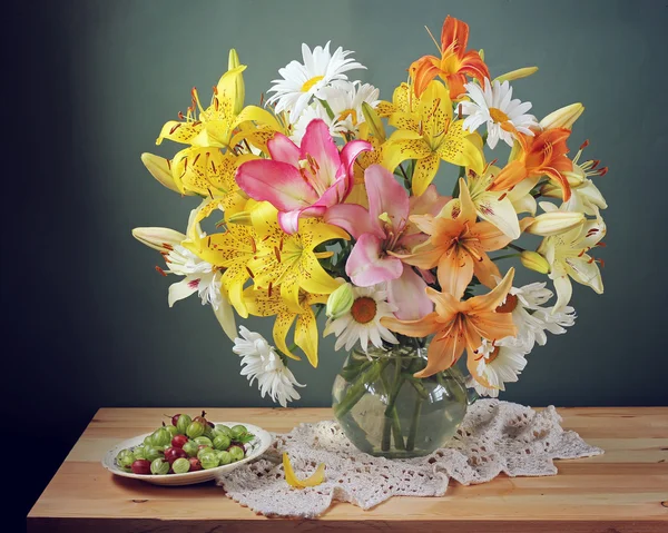 Still life with bouquet of lilies in glass jug on a blue backgro