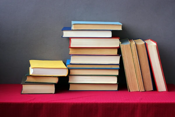 A stack of books on the table with a red tablecloth.