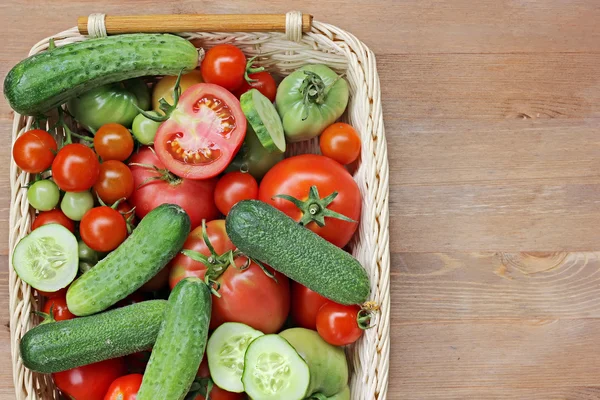 Fresh cucumbers, red and green tomatoes in a basket on a table