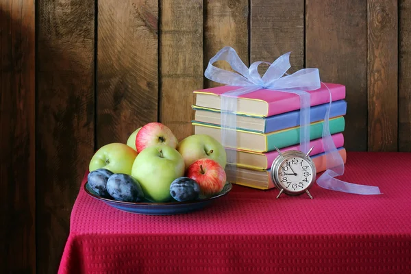 A still life with books, plums and apples,  back to school.