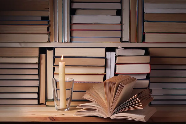The opened book and the burning candle against from books.