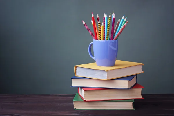 Pile of books with color covers and colored pencils in a cup.
