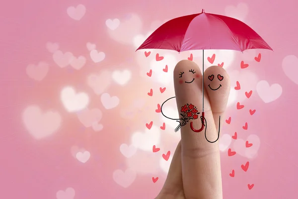 Conceptual finger art. Lovers is embracing and holding red umbrella with falling hearts. Stock Image