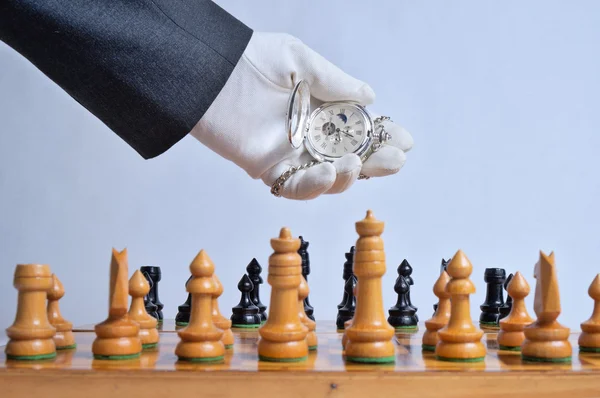White glove holding a pocket watch above a chessboard