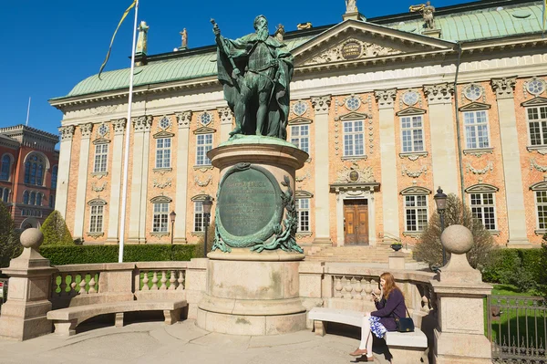 Lady relaxes at the bench in front of the House of Nobility and statue of Gustaf Eriksson Vasa in Stockholm, Sweden.