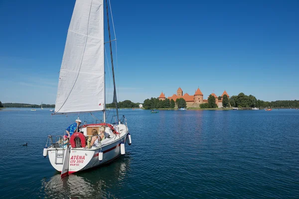 People enjoy boat trip at Galve lake with the Trakai castle at the background on a hot summer day in Trakai, Lithuania.