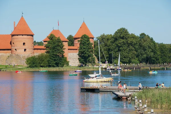 People sunbathe at Galve lake with the Trakai castle at the background on a hot summer day in Trakai, Lithuania.