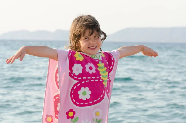 Beautiful little girl smiling at seaside in pink butterfly towel