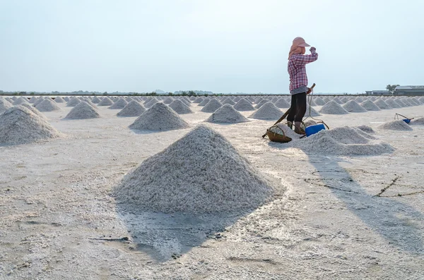 Worker standing at salt field that has pile of sea salt.