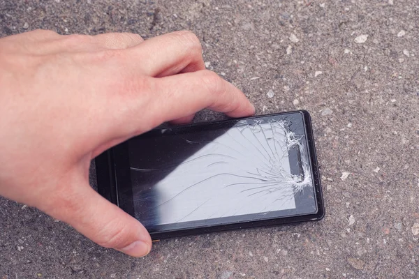 Person picking up a cracked smartphone