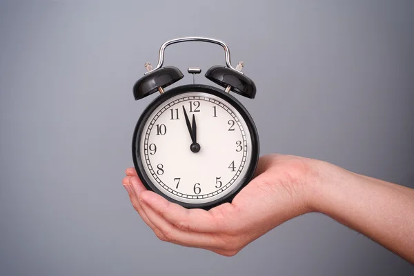 Classic alarm clock in woman hand against grey background