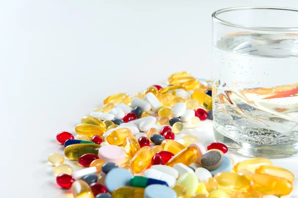 Colorful pills and glass of water, on white background