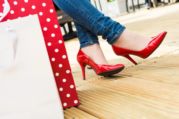 Attractive young female in sexy red high heels enjoying a break after successful shopping, detail shot, with copy space