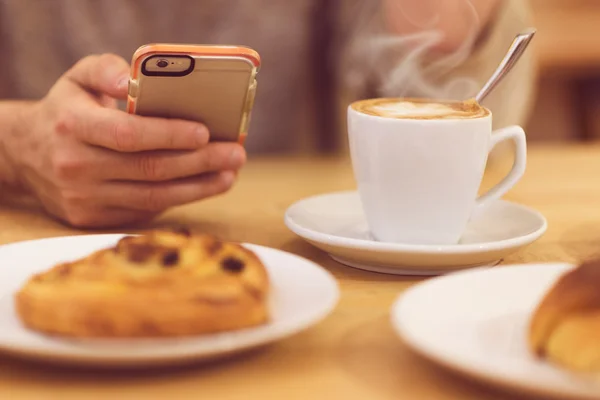 Always in touch. Detail image of unrecognizable man drinking coffee and holding smart phone while having breakfast in restaurant.