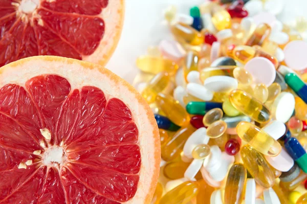 Pink grapefruit and pills, vitamin supplements on white background with copy space, healthy diet concept