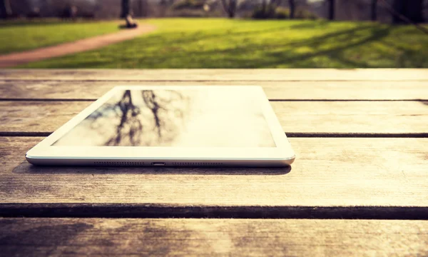 Rustic wooden table with digital tablet and trees reflecting on black screen. View from above with copy space