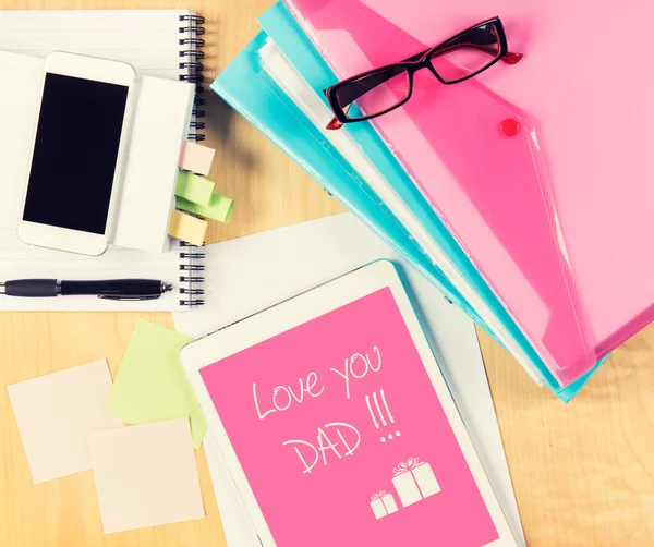 Messy office table with Fathers day card on digital tablet. View from above with copy space