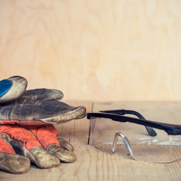 Old used safety glasses and gloves on wooden background