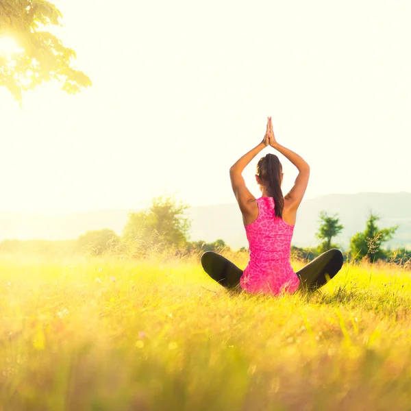 Young athletic woman practicing yoga on a meadow at sunset, image with lens flare