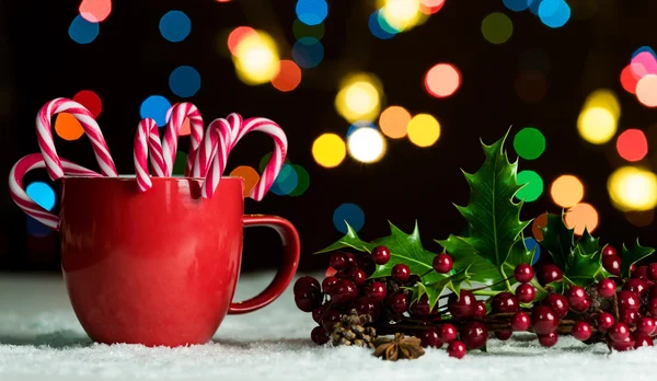 Red mug with candy canes in snow with defocussed fairy lights, bokeh in the background, Festive Christmas background