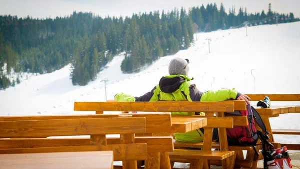 Skier sitting in an outdoor bar in a ski resort, enjoying views
