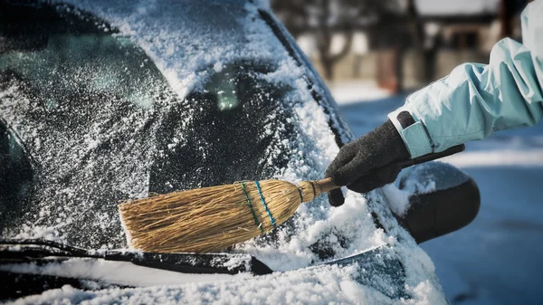 Transportation, winter, weather, people and vehicle concept - woman cleaning snow from her car with a broom